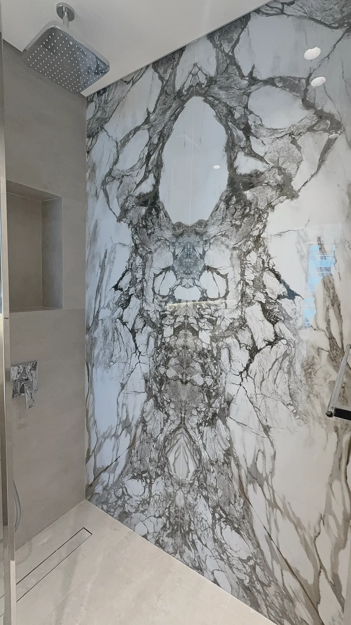 Marina Apartment walk-in shower with bookmatched marble wall and rain shower head