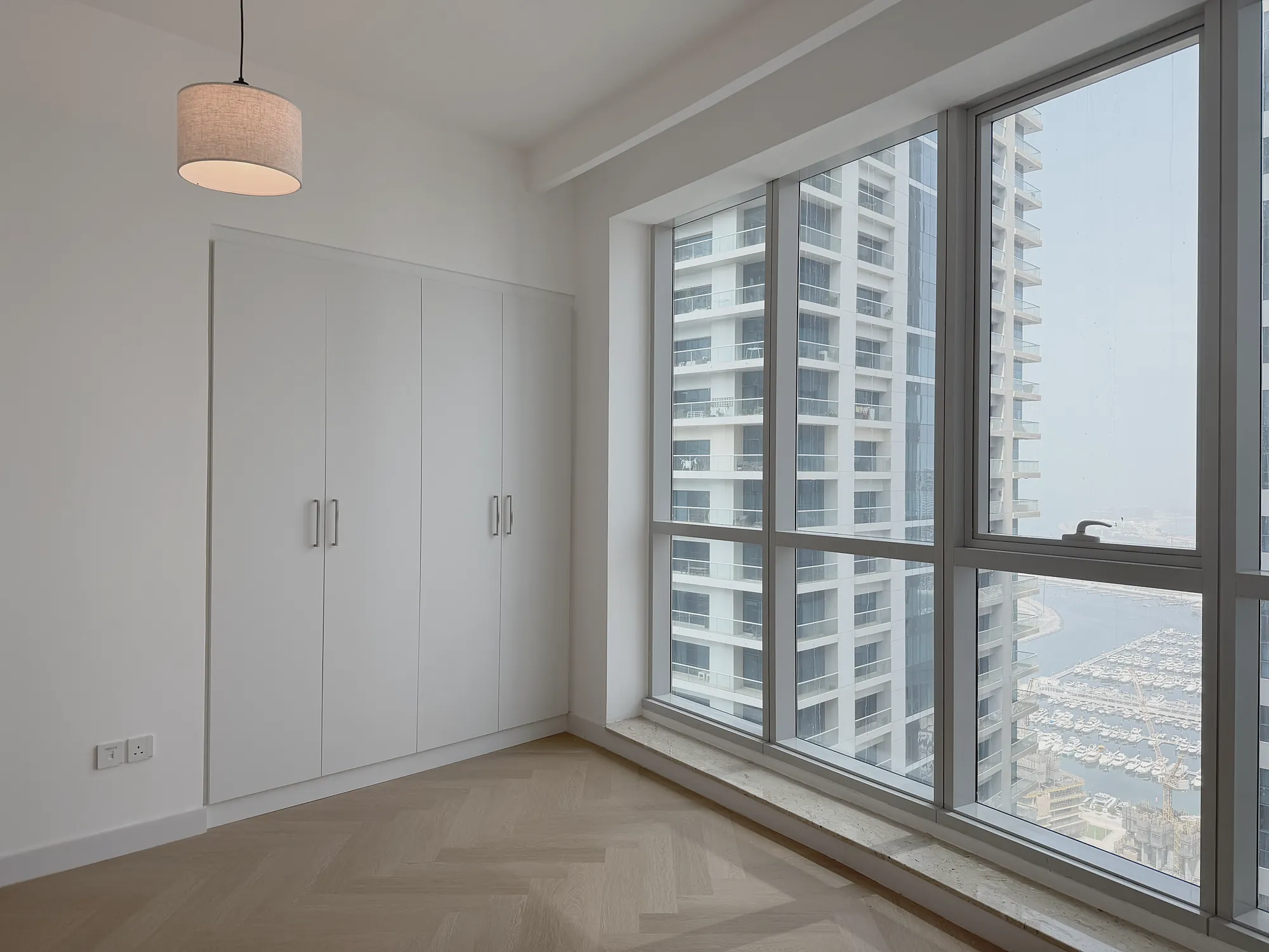 Marina Apartment bedroom with built-in wardrobe, herringbone oak floor and full-height glazing over Dubai Marina